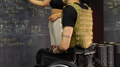 a man sitting on a wheelchair while listening to the woman writing on the board