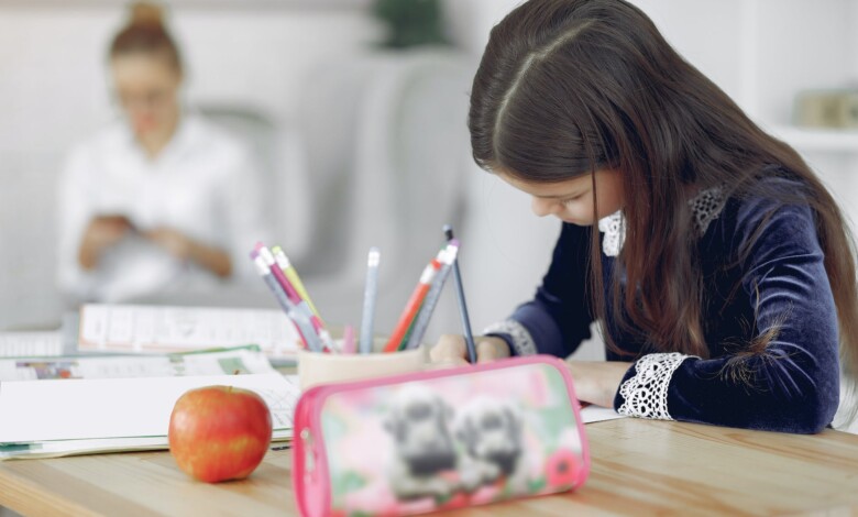 little girl studying at table near mother in living room