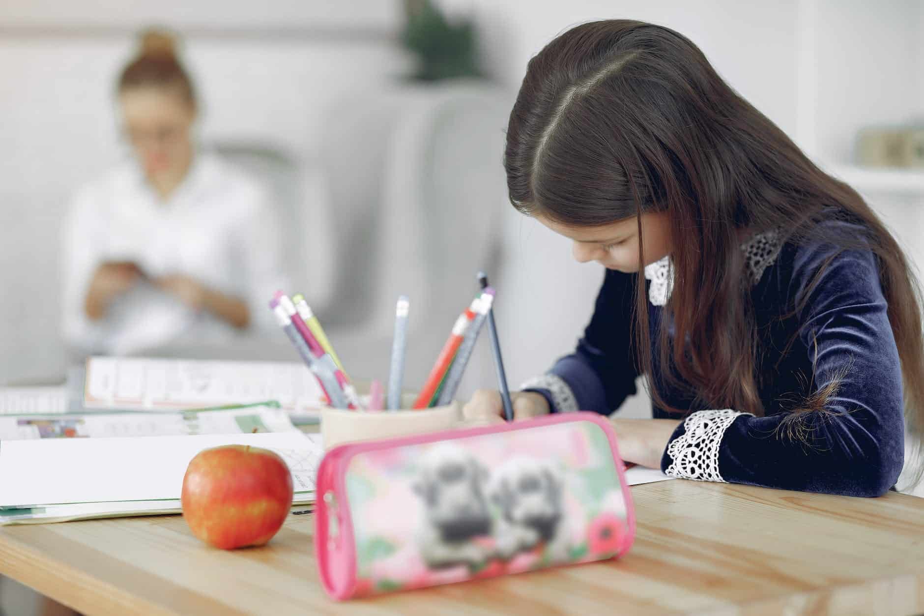 little girl studying at table near mother in living room
