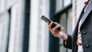 crop businesswoman messaging on smartphone while standing near building on street