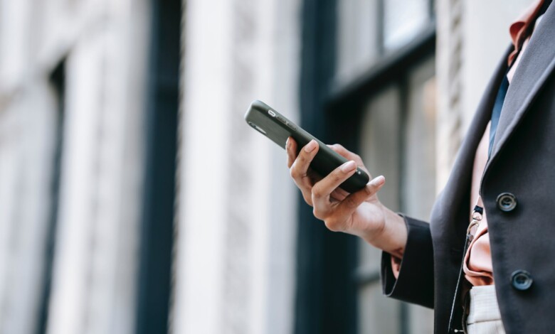 crop businesswoman messaging on smartphone while standing near building on street