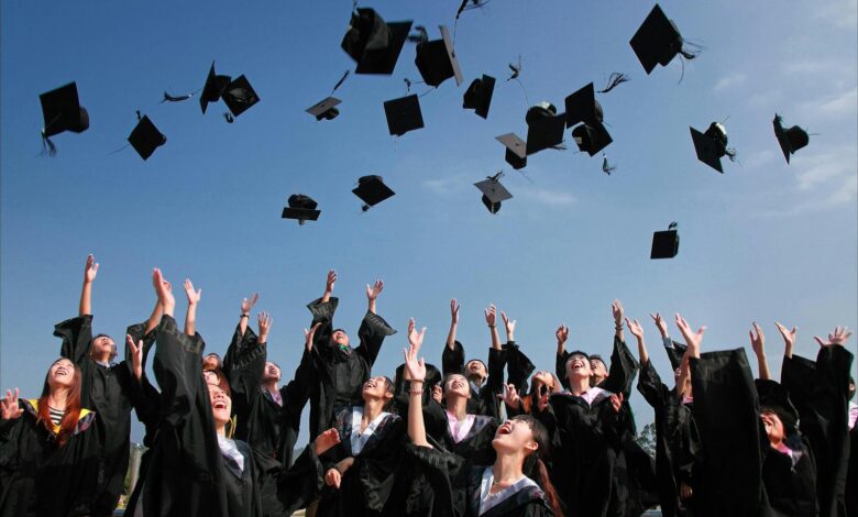 newly graduated people wearing black academy gowns throwing hats up in the air