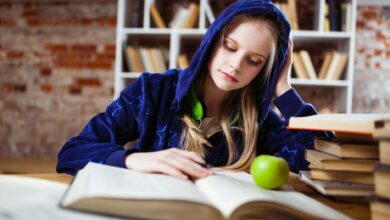 woman wearing blue jacket sitting on chair near table reading books