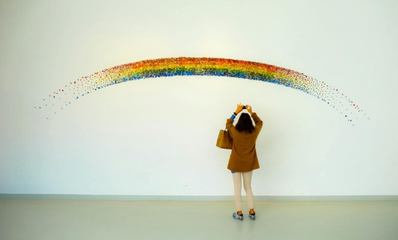 woman wearing brown top and beige leggings taking picture rainbow painted wall