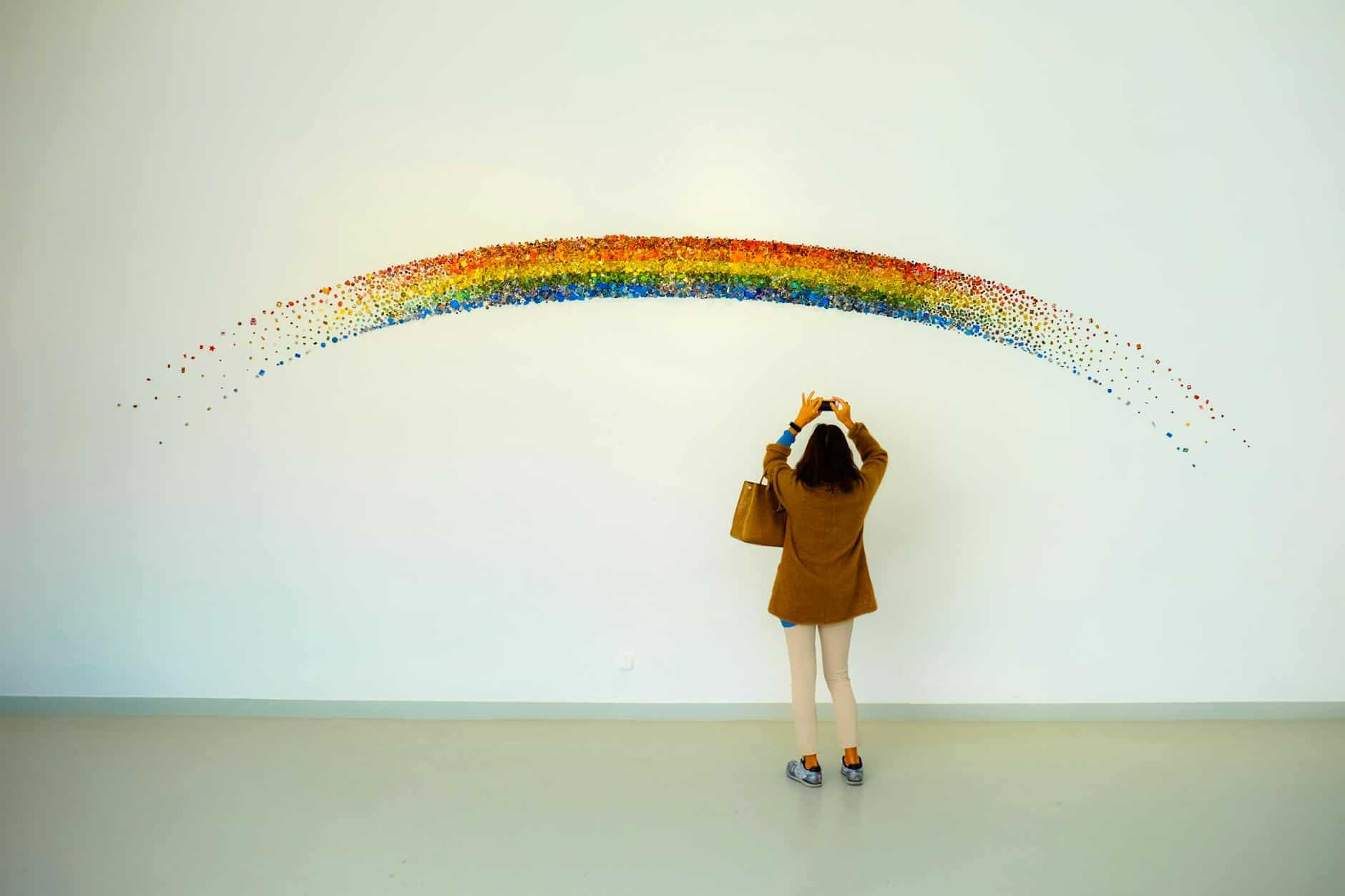 woman wearing brown top and beige leggings taking picture rainbow painted wall