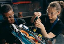 woman in black shirt wearing protective goggles holding black and green screw driver