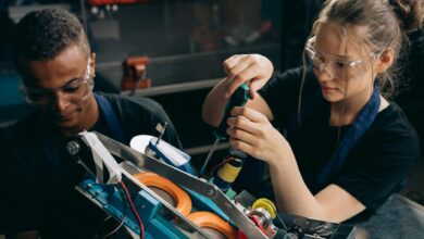 woman in black shirt wearing protective goggles holding black and green screw driver
