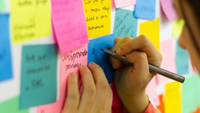 person writing on pink sticky notes