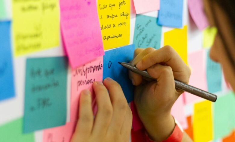 person writing on pink sticky notes