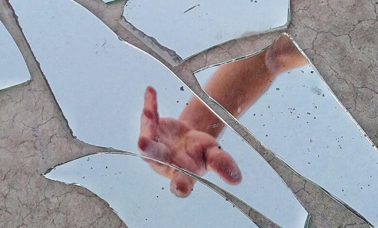 mirror fragments on gray surface with the reflection of a person s hand