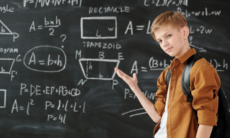 boy in brown jacket standing in front of chalk board