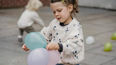 crop girl with balloons on pavement near unrecognizable friend