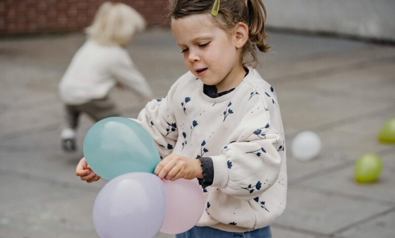 crop girl with balloons on pavement near unrecognizable friend