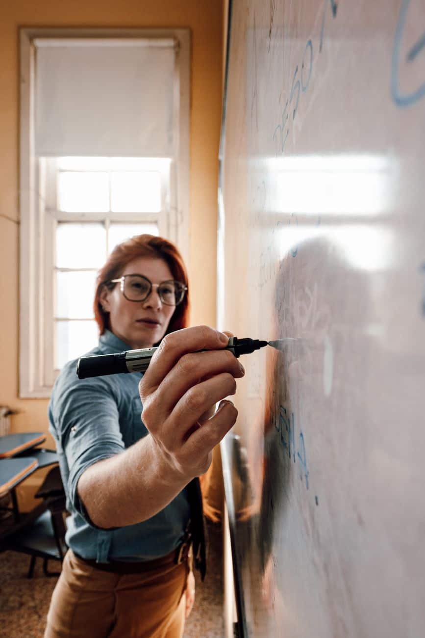 female teacher writing on whiteboard in classroom