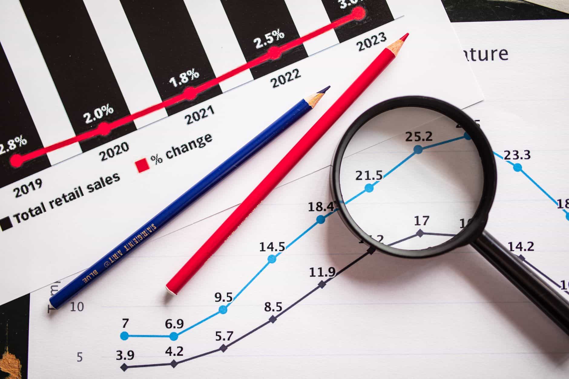 colored pencils and a magnifying glass over documents with graphs
