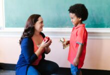 a teacher looking at her student while holding an apple