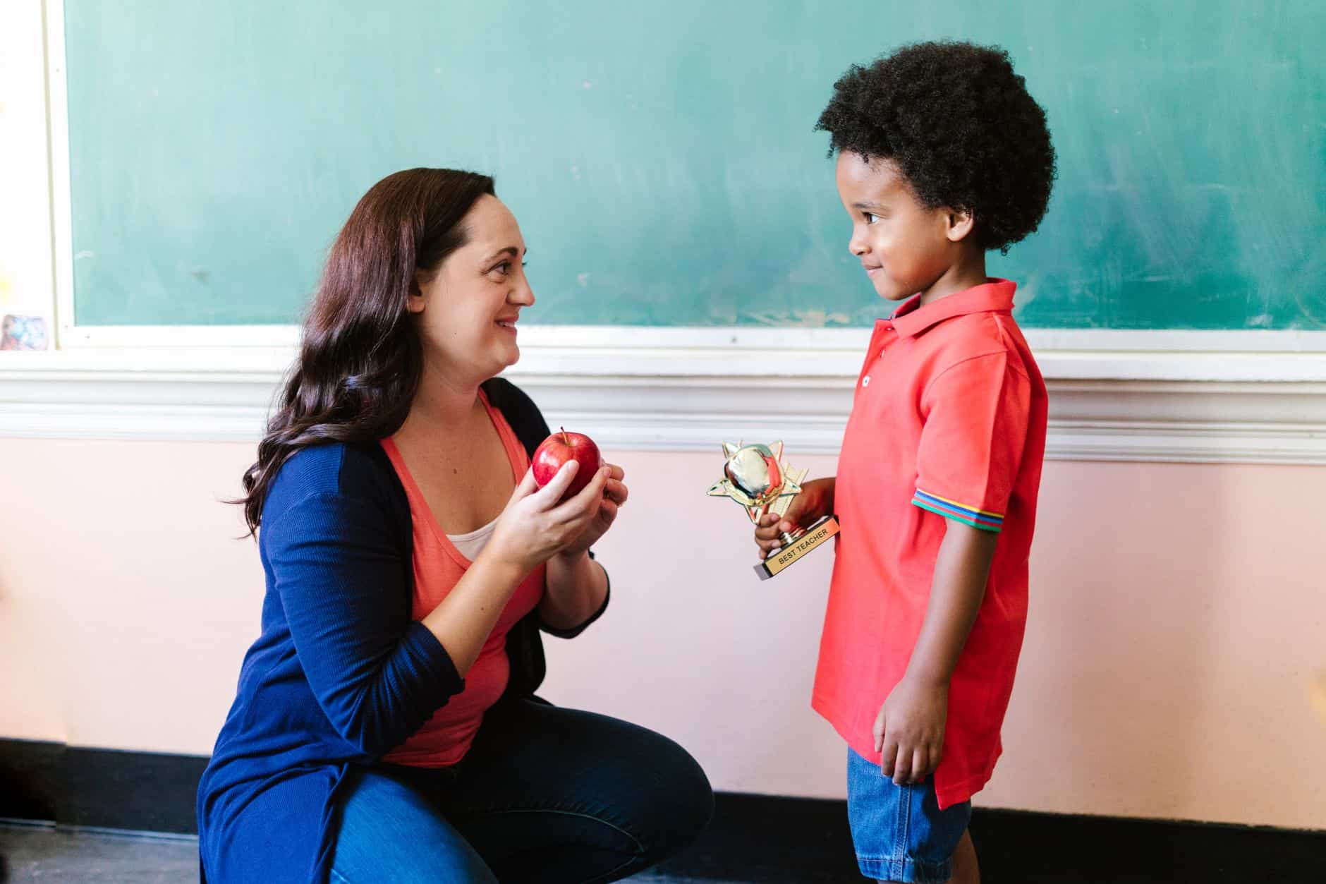 a teacher looking at her student while holding an apple