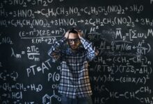 man in eyeglasses holding his head next to blackboard with math equations