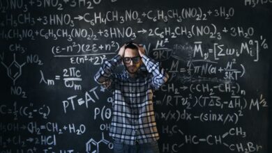 man in eyeglasses holding his head next to blackboard with math equations